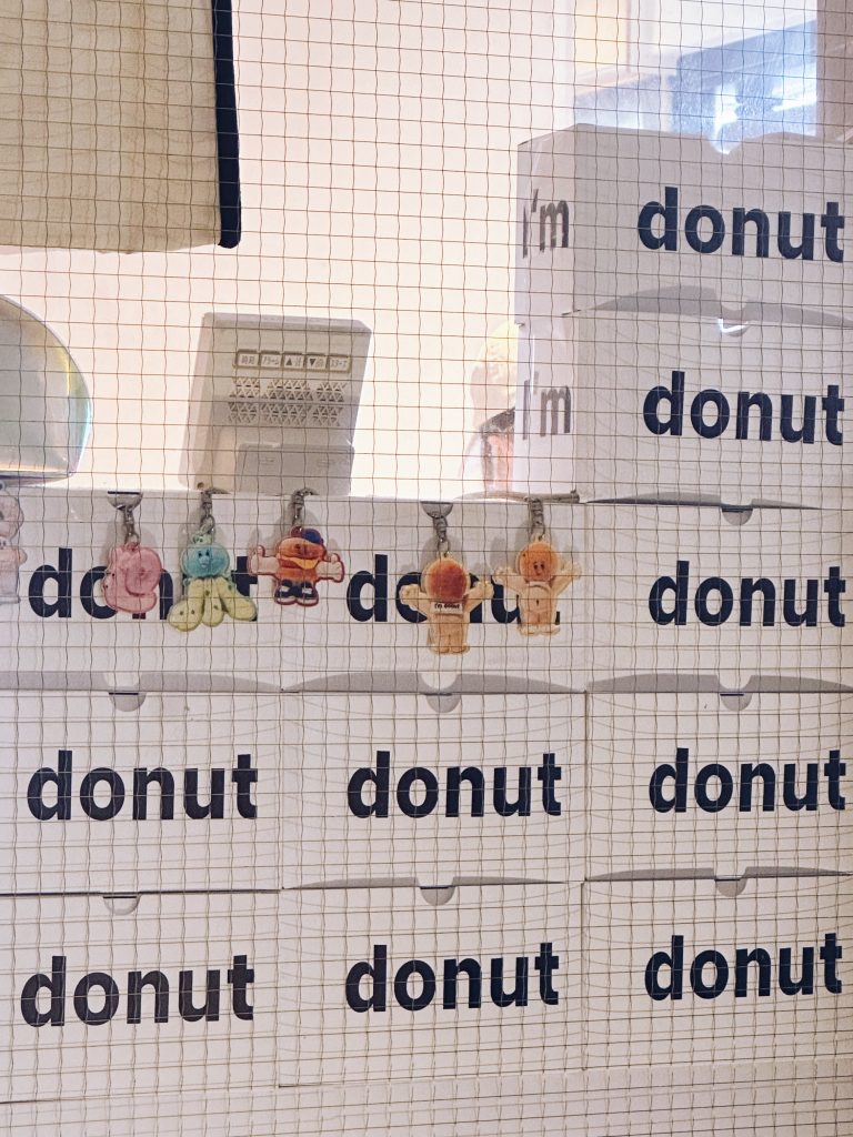 東京甜甜圈店內部陳列，多個甜甜圈外帶盒堆疊，透過玻璃與網格拍攝，呈現日常販售場景