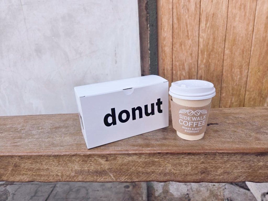 東京街邊咖啡店的外帶咖啡與甜甜圈盒，放置在木質長椅上，呈現日常咖啡時光